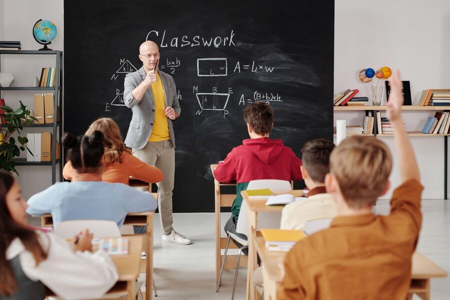 A teacher at the blackboard with pupils raising their hands